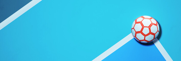 White orange futsal soccer ball in the corner of a blue indoor soccer field background