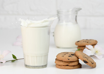 full glass cup of fresh milk with splashes stands on a white table, healthy breakfast