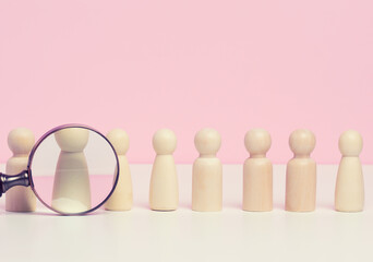 wooden figures of men stand on a pink background and a red plastic magnifying glass. Recruitment concept, search for talented and capable employees