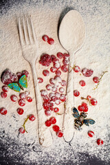 A spoon and a fork, red berries are sprinkled with flour and a brochure in the form of insects lies at the top. Creative food preparation.