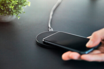 Man placing smartphone on induction wireless charger in office. Grey desk surface background.