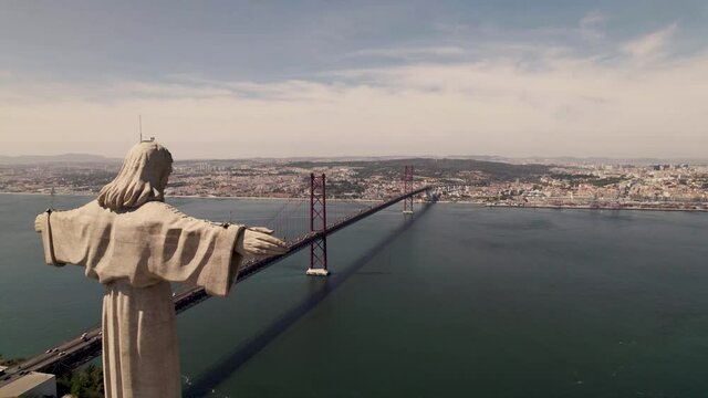 Panoramic orbiting shot around the statue of Christ the King overlooking Lisbon cityscape.
