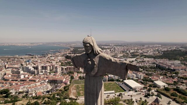Aerial pan right shot of front facing of Christ the King with Almada cityscape background, Portugal.