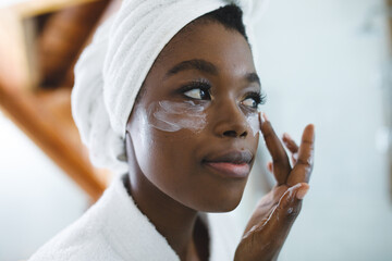 Smiling african american woman in bathroom applying face cream for skin care