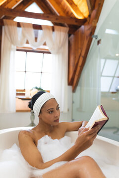 Mixed race woman in bathroom, relaxing in bath reading book
