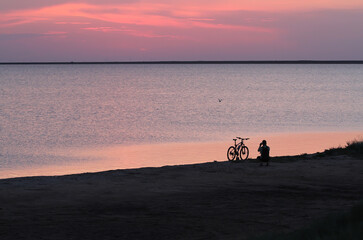 The man next to the bike is filming the sunset near the water