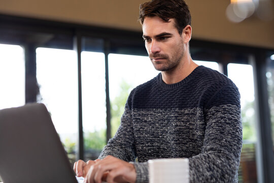 Caucasian man sitting at table in kitchen working remotely using laptop