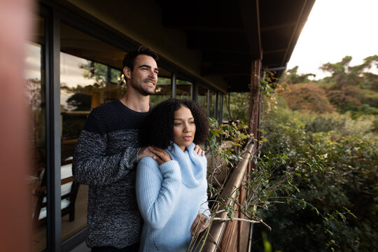 Happy diverse couple on balcony together embracing talking and smiling
