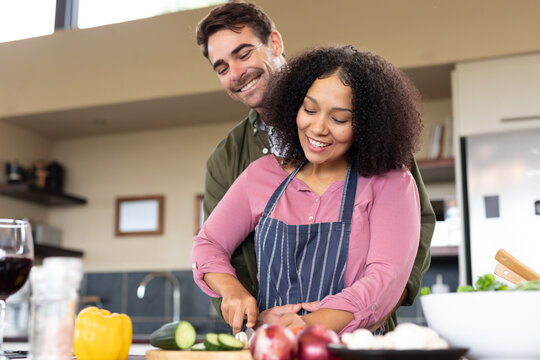 Happy diverse couple in kitchen preparing food together chopping vegetables