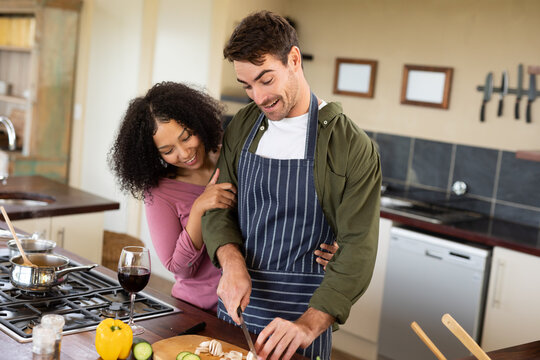Happy diverse couple in kitchen preparing food together chopping vegetables