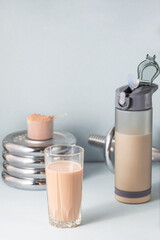 Healthy food concept. Protein drink.
 There is a sports bottle, a glass with a cocktail, dumbbells in the background, a measuring spoon with a dry additive.