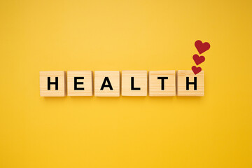 HEALTH word is written on wood blocks with three red heart symbols isolated on a yellow background. Top view. Close-up photo. Health and healthcare concept