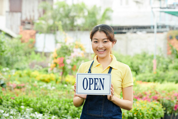 Portrait of happy exited female city garden worker showing open sign