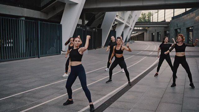 Diverse group of six stylish professional dancers performing a zumba dance routine in front of city view. Fitness, sport, dance and lifestyle concept - group of smiling women with coach dancing zumba