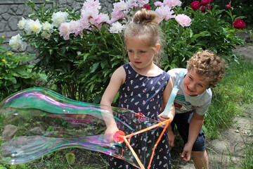 Girl and boy play soap bubbles on a background of flowers