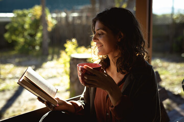 Mixed race woman reading book and drinking coffee in sunny garden