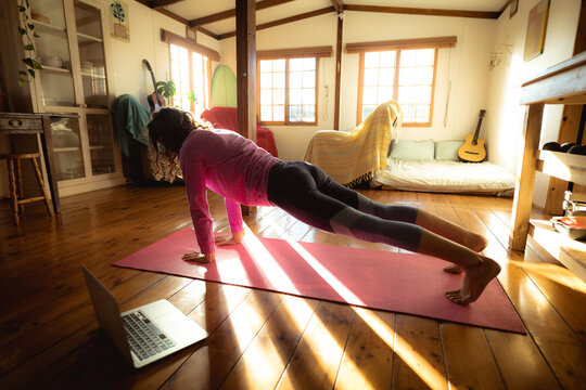 Mixed race woman practicing yoga, doing push ups in sunny living room