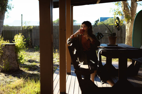Mixed race woman sitting and drinking coffee in sunny garden