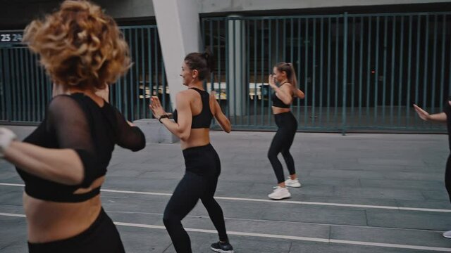 Rear view a group of girls under the guidance of a trainer perform a set of aerobics exercises and dance zumba. Outdoor morning warm-up