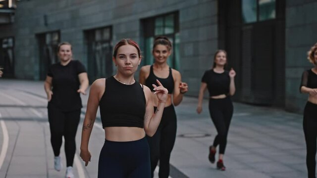Smiling zumba class dancing in the city at night time. People in black sportswear training sports activities outdoors in summer evening