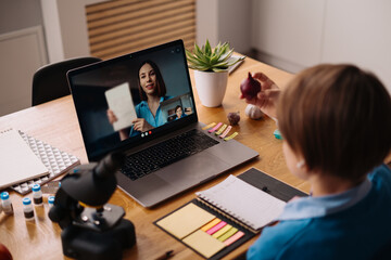 A Preteen boy uses a laptop to make a video call with his teacher. The Screen shows an online lecture with a teacher explaining the subject from class.