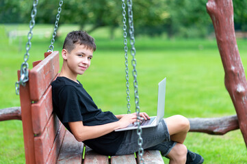 Boy with using laptop on the swing. First time to school. Outdoor learning concept