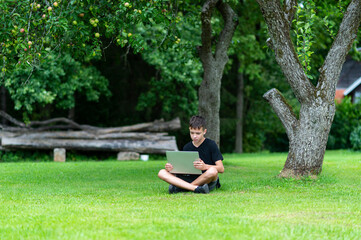 Boy with using laptop on green grass. First time to school. Back to school. Outdoor learning concept