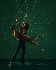 Two young ballet dancers, man and woman dancing in the raindrops over dark background. Art, action,...