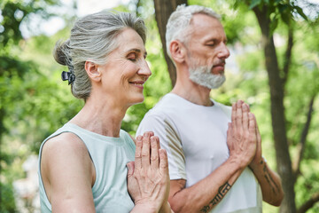 Pensioners working out and standing with prayer gesture while feeling as relaxed