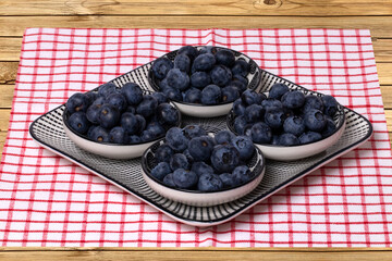 Closeup of a decorative plate with four bowls with fresh blueberries on a rustic wooden table. Concept of healthy nutrition. Space for your design.
