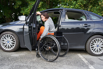 Plakat Disabled woman sitting on wheelchair boarding into her car