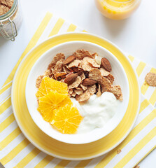 Whole grain oats and wheat flakes with orange, almond nuts and yogurt in a white bowl. Healthy morning breakfast concept close up