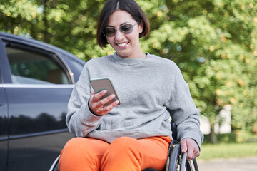 Girl with lower body disability sitting at wheelchair near her car and checking messages