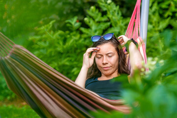 gorgeous female with sunglasses lying in a hammock in the garden and relaxing, selective focus