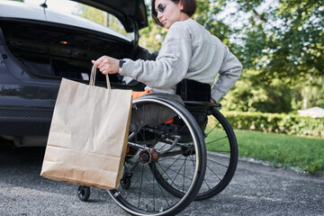 Handicapped woman at the wheelchair holding her purchases and putting shopping bag
