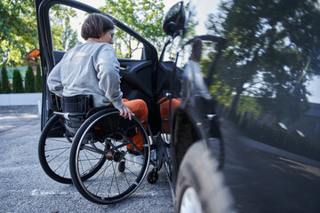 Young girl with lower body disability switches position from the wheelchair into the car