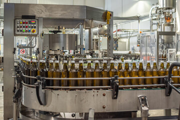 Brown glass bottles of drinking water on a conveyor belt move into a labeling machine