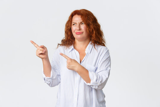 Skeptical And Disappointed Redhead Middle-aged Woman, Mother Dislike Promo Banner, Pointing And Looking Upper Left Corner And Grimacing Judgemental, Standing White Background