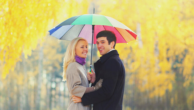 Portrait of happy smiling young couple with colorful umbrella in warm sunny day on yellow leaves background