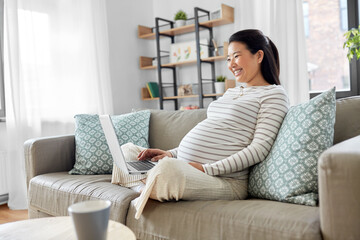 Obraz na płótnie Canvas pregnancy, rest, people and expectation concept - happy smiling pregnant asian woman with laptop computer sitting on sofa at home