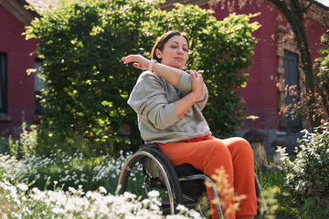Brunette girl with loss of leg function sitting at the wheelchair and stretching her arms
