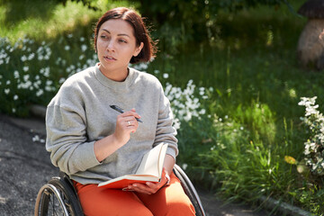 Woman with lower body disability sitting at wheelchair and pondering while writing