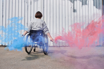 Woman riding at the wheelchair and holding bombs with colored smoke while enjoying