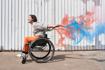 Woman with lower body disability riding at the wheelchair while holding bombs with smoke - obrazy, fototapety, plakaty