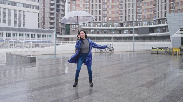 Young asian woman dancing with umbrella in rain, enjoying weather, good mood