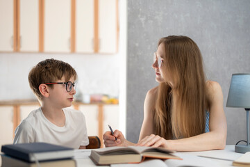 Fototapeta premium Mother explains to her son how to do his homework. Young tutor works with a student. Home schooling.