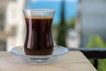 Turkish coffee in transparent traditional glass against buildings and sea view with trees in summer
