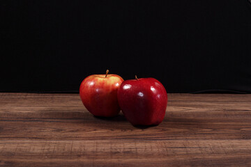 Manzanas rojas y verdes sobre madera rustica oscura y fondo negro.