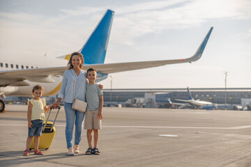 Full length shot of happy mother with two little kids smiling at camera while standing in front of...