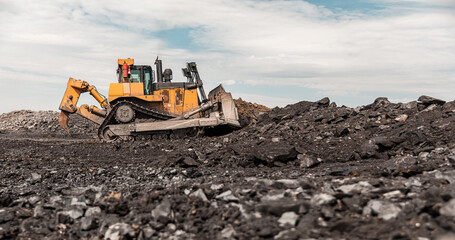 Yellow excavator in career moves overburden. Bulldozer combs the ground, with the bright sun and nice blue sky in the background